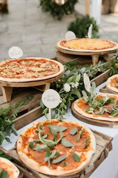 several pizzas are on wooden trays with greenery and place cards in front of them