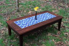 a wooden table with blue and white tiles on it in the grass next to trees