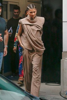 a woman is walking down the street with her hair in a ponytail and wearing a brown outfit