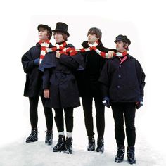 four men in black coats and hats are standing on the snow with their hands together