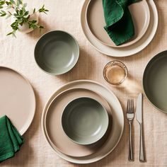 the table is set with plates, silverware and green napkins