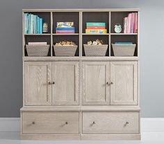 a bookcase with baskets and books on top of it in front of a gray wall