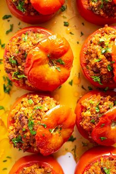 several stuffed tomatoes are arranged on a yellow surface with parsley sprinkled around them