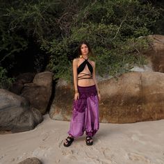 a woman standing on top of a sandy beach next to some rocks and trees in the background