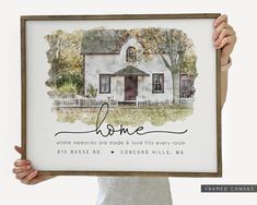 a woman holding up a framed poster with the words, home and a house on it