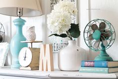 a white mantle topped with books and vases filled with flowers next to an alarm clock