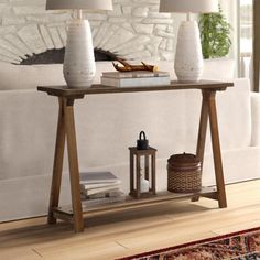 a table with two lamps on it in front of a white couch and rugs