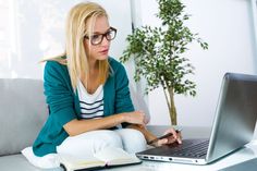 a woman is sitting on the couch with her laptop and looking at something in front of her