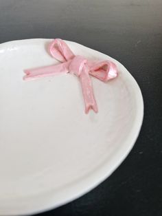 a white plate with a pink bow on it sitting on a black table top next to a cup