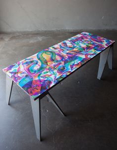 a colorful table sitting on top of a cement floor next to a wall in an empty room