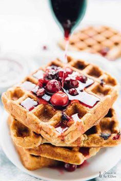 a stack of waffles with syrup and cherries on top sitting on a white plate