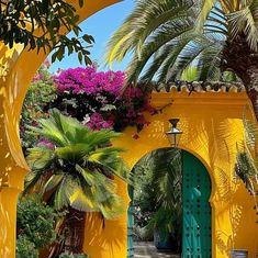 a yellow building with green doors and flowers on the outside, surrounded by palm trees