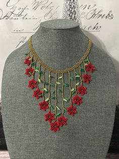 a necklace with red flowers and green leaves is displayed on a mannequin head