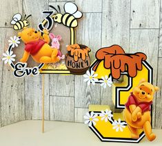 a winnie the pooh cake topper on a stick with flowers and bees around it