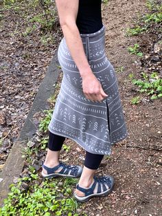 a woman standing in the woods with her hand on her hip, wearing sandals and a skirt