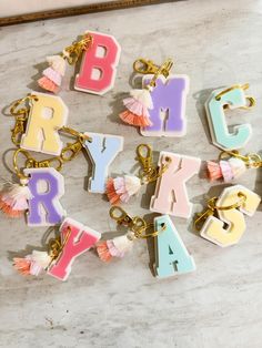 letters and tassels are arranged in the shape of keychains on a marble surface