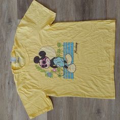 a yellow shirt with mickey mouse on it sitting on a wooden floor next to a pair of scissors