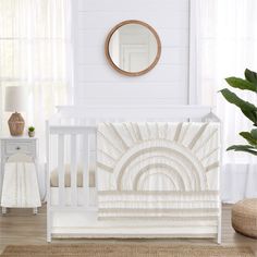 a white crib bedding set with a sun design in the middle and a round mirror above it