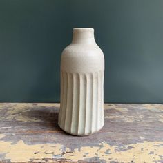 a white vase sitting on top of a wooden table next to a green painted wall