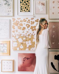 a woman standing in front of a wall covered with pictures and art on it's walls