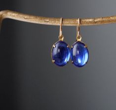 "Gorgeously smooth vintage sapphire blue glass is set in a closed-backed pronged setting.  Gorgeous, unique, elegant earrings that move and catch the light. * Each vintage sapphire glass pendant is 1/2 inch long and about 1/4 inch wide.  * Glass cabs are vintage, likely from the 40s, with undamaged foil backs that reflect the light * unfinished brass prong setting is new * 14K gold fill earring backs are new. Set in brass and hung from new 14k gold fill French loop ear wires or 14k gold fill lev Blue Cabochon Earrings For Formal Occasions, Elegant Blue Oval Cabochon Earrings, Elegant Blue Cabochon Earrings, Elegant Sapphire Jewelry With Cabochon, Blue Cabochon Drop Jewelry, Blue Drop Cabochon Jewelry, Blue Drop Jewelry With Cabochon, Blue Oval Cabochon Formal Jewelry, Classic Sapphire Drop Jewelry