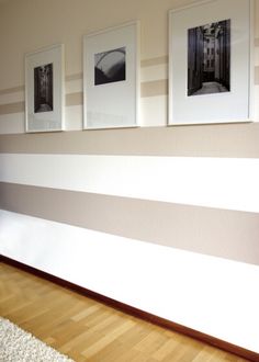 three framed pictures hang on the wall above a wooden floor in front of a striped wall