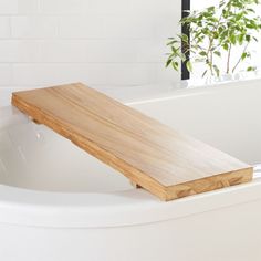 a wooden bench sitting on top of a white bath tub next to a green plant