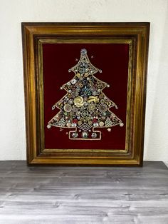 a christmas tree made out of buttons in a gold frame on top of a wooden table