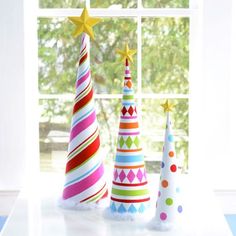 three brightly colored christmas trees sitting on top of a table next to a window sill