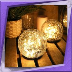 two lit up balls sitting on top of a wooden table next to candles and potted plants