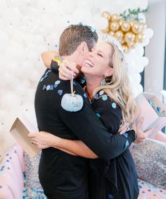 a man and woman hugging each other in front of a balloon wall with confetti on it