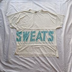 "Vintage 80s SWEATS dd Bi Chego white and blue t-shirt. Size medium, fits oversized. Single stitch. 65% polyester, 35% cotton. Flaws: One dark mark on the front. Note: Longer in back by like half an inch. Care: Machine washable. Measurements  Length: 24.5\" Width: 22\"" Oversized Hip Hop Tops With Letter Print, White Boxy Fit T-shirt With Letter Print, White Boxy Fit T-shirt With Text Print, Sporty Boxy Fit T-shirt For Loungewear, Crew Neck Logo T-shirt For Loungewear, White Crew Neck T-shirt For Leisure, Graphic Print Drop Shoulder Tops For Loungewear, Drop Shoulder Graphic Print Tops For Loungewear, Oversized White Hip Hop Sweatshirt