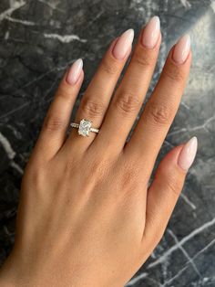 a woman's hand with a diamond ring on her left hand, against a marble background