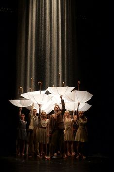 a group of people standing under umbrellas in the rain with their hands raised up