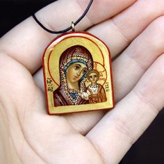 a hand holding a wooden pendant with an image of the virgin mary and child jesus