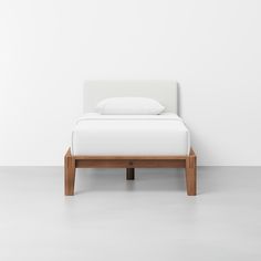 a bed with white sheets and pillows on top of it, against a white wall