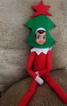 an elf doll sitting on top of a couch wearing a green hat and red pants