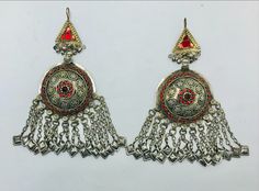 * This astonishing handpicked pair of tribal vintage earrings is a traditional ornament, stylish and classy both. * The unique ethnic earrings are hand embellished with red glass stone inlays and finely carved archaic patterns, while the bottom of the pair is ornated with long dangling tassels. The elegant earrings are made with metal alloy and covered with rustic silver hues, flaunting all the tribal kuchi vibes. * These nomadic earrings are there to be styled in a truly wonderful way to stun o