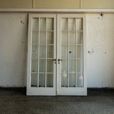 two white double doors with glass panes in an empty room next to a wall