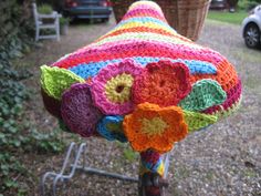 a colorful crocheted hat is hanging from a tree in front of a car