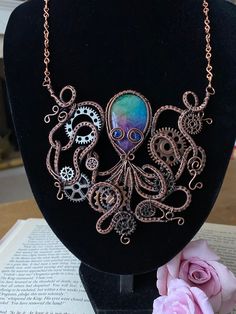 Dive into the enchanting world of steampunk with this wire-woven octopus necklace, where creativity meets craftsmanship. The centerpiece features a captivating rainbow agate, surrounded by meticulously incorporated cogs and gears, echoing the essence of industrial allure. The hand-woven bib necklace showcases a unique design that seamlessly marries artistry and steampunk aesthetics. Adorn yourself with this distinctive accessory, a wearable masterpiece that captures the intrigue of the deep sea Multicolor Metal Wire Wrapped Necklaces, Multicolor Wire Wrapped Metal Necklaces, Handmade Mystical Multicolor Jewelry, Handmade Adjustable Fantasy Necklaces, Handmade Multicolor Fantasy Jewelry, Steampunk Adjustable Necklace With Soldered Details, Adjustable Steampunk Copper Jewelry, Handmade Steampunk Copper Jewelry, Adjustable Copper Steampunk Jewelry