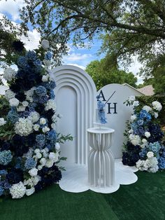 a white table surrounded by blue and white flowers in front of a sign that says ah