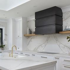 a kitchen with white cabinets and marble counter tops, gold faucets and brass pulls