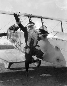 santa claus standing on the wing of an old fashioned airplane with his arms in the air