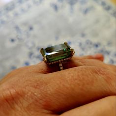 a person's hand holding an emerald ring