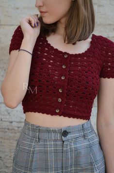 a woman wearing a red crochet crop top and plaid skirt with her hand on her chin