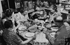 a group of people sitting at a table eating food together in a kitchen with pots and pans on the stove