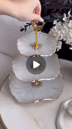 three tiered tray with white flowers on it and a person holding a gold ring