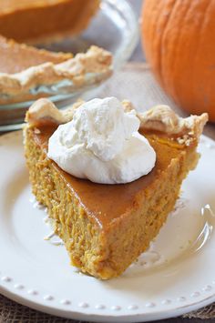 a slice of pumpkin pie on a white plate with whipped cream in the middle and an orange pumpkin behind it