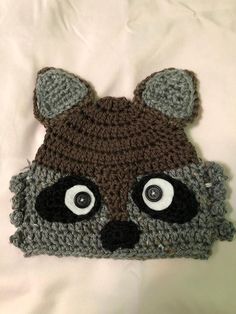 a crocheted raccoon hat with big eyes on top of a white sheet